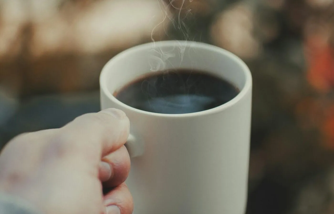Manos sosteniendo una taza caliente con luz cálida de fondo